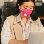 Woman in an office wearing a pink face mask, focused on work at her desk.